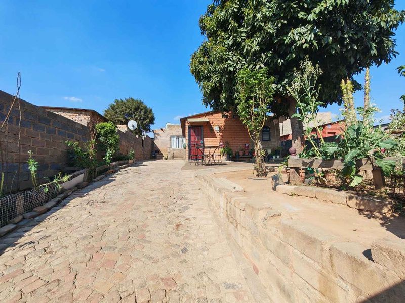 Rear exterior view of the property featuring a paved courtyard, boundary walls, and an exposed brick building facade.