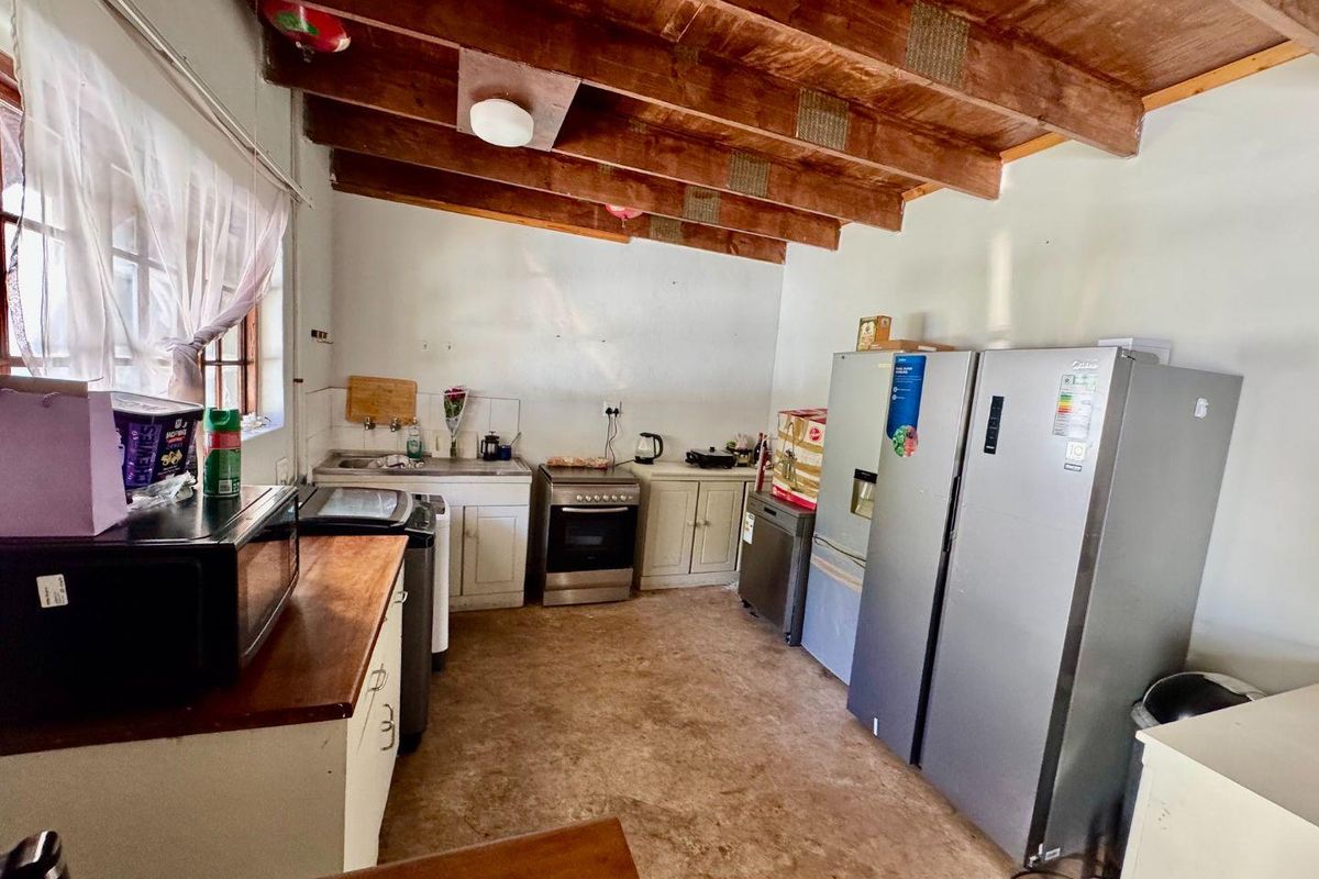 A functional kitchen area featuring exposed timber ceiling beams, built-in cabinetry, a freestanding stove, and a stainless steel sink.