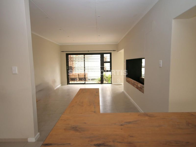 Spacious open-plan living area featuring tiled floors, a built-in fireplace, and a breakfast bar, leading out through a security gate to the exterior.