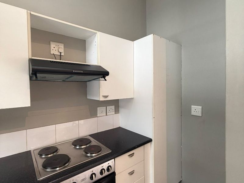 Compact kitchen featuring white cabinetry, a built-in oven with electric hob, extractor fan, and tiled flooring.