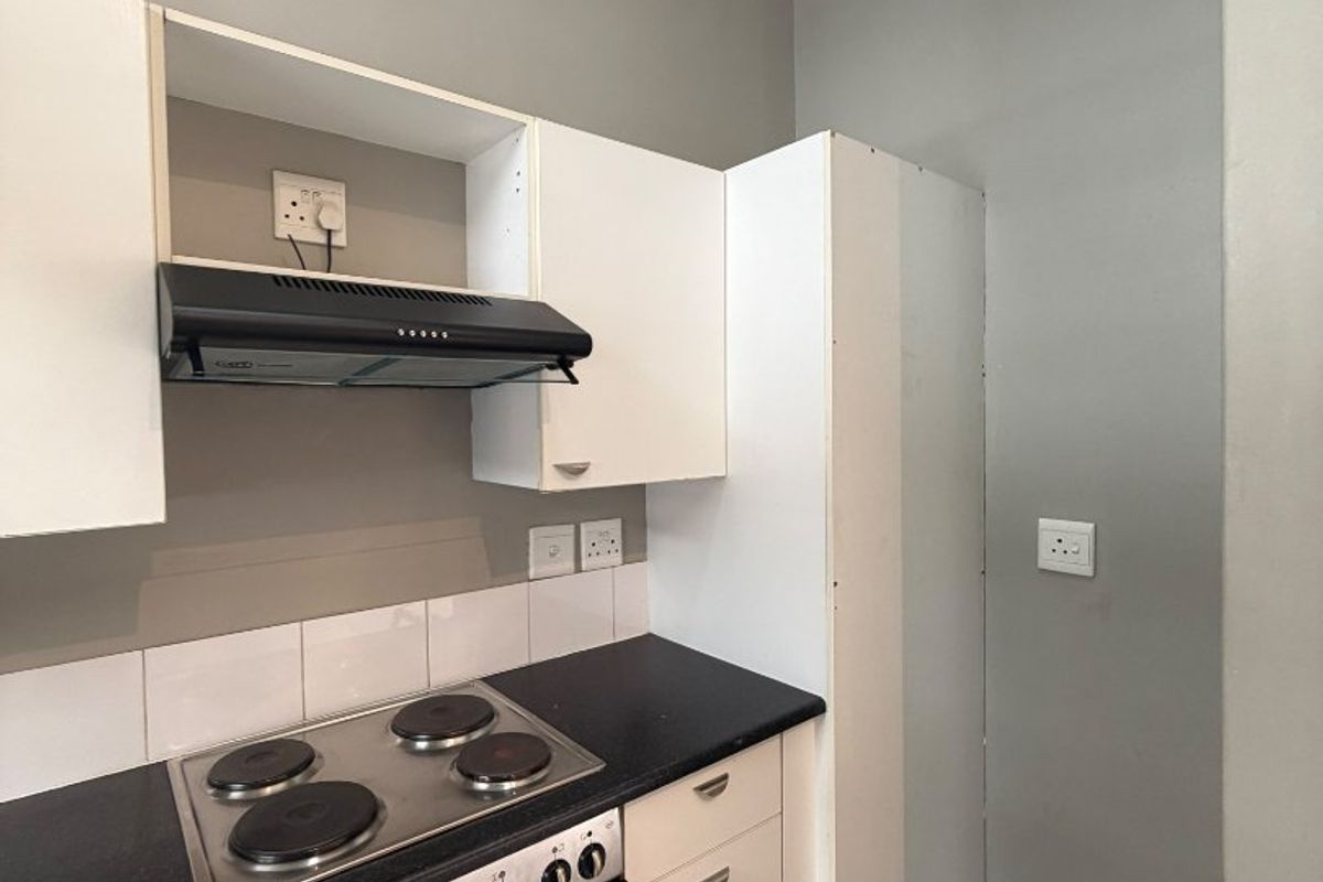 Compact kitchen featuring white cabinetry, a built-in oven with electric hob, extractor fan, and tiled flooring.