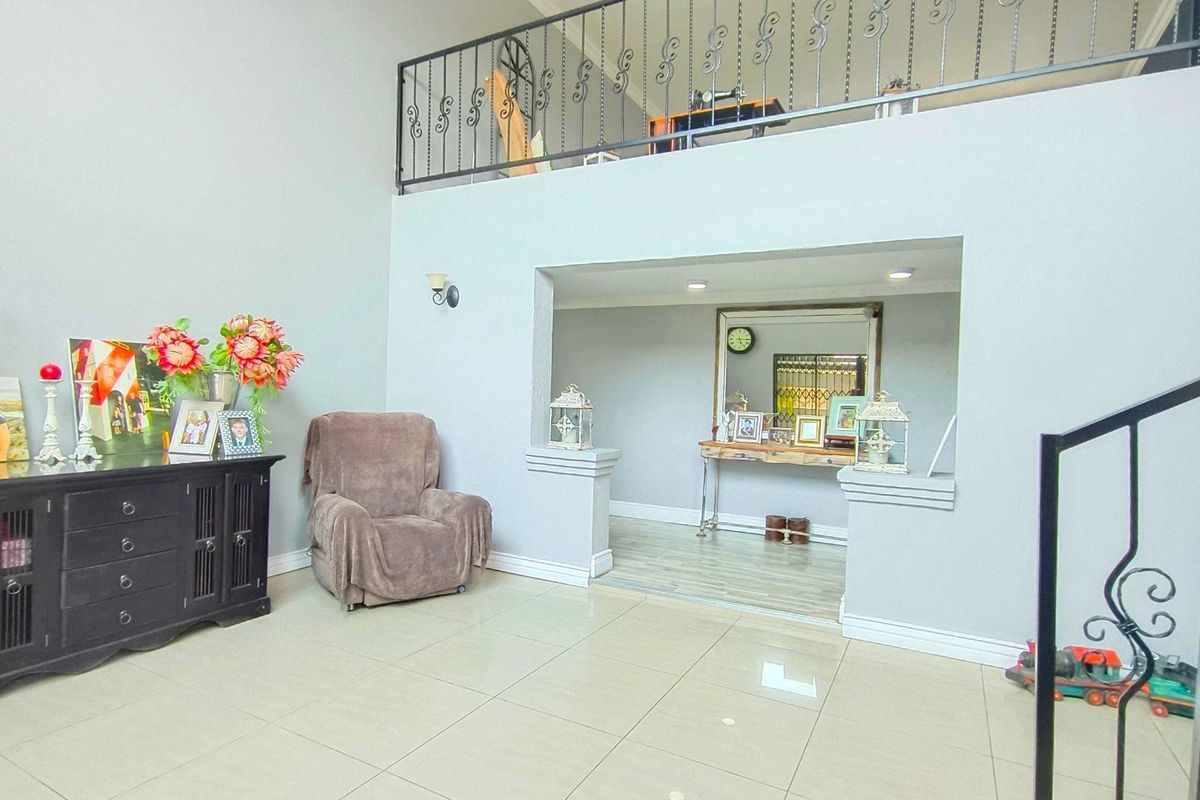 Spacious living area featuring high ceilings, tiled flooring, and a mezzanine level with decorative wrought iron railings.