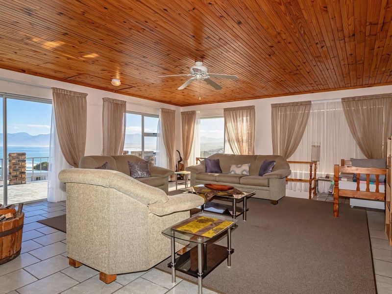Spacious living room featuring a warm timber-clad ceiling, tiled flooring, and large sliding doors that open to expansive coastal views.