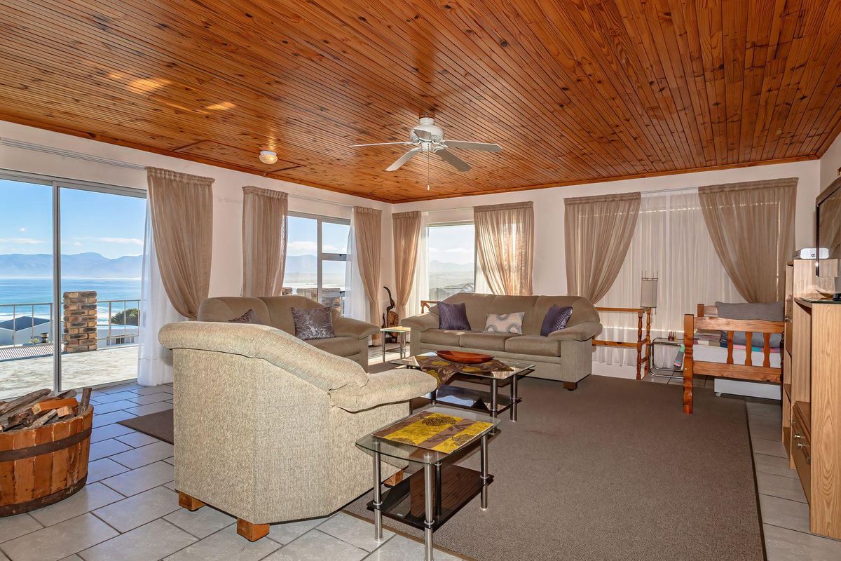 Spacious living room featuring a warm timber-clad ceiling, tiled flooring, and large sliding doors that open to expansive coastal views.