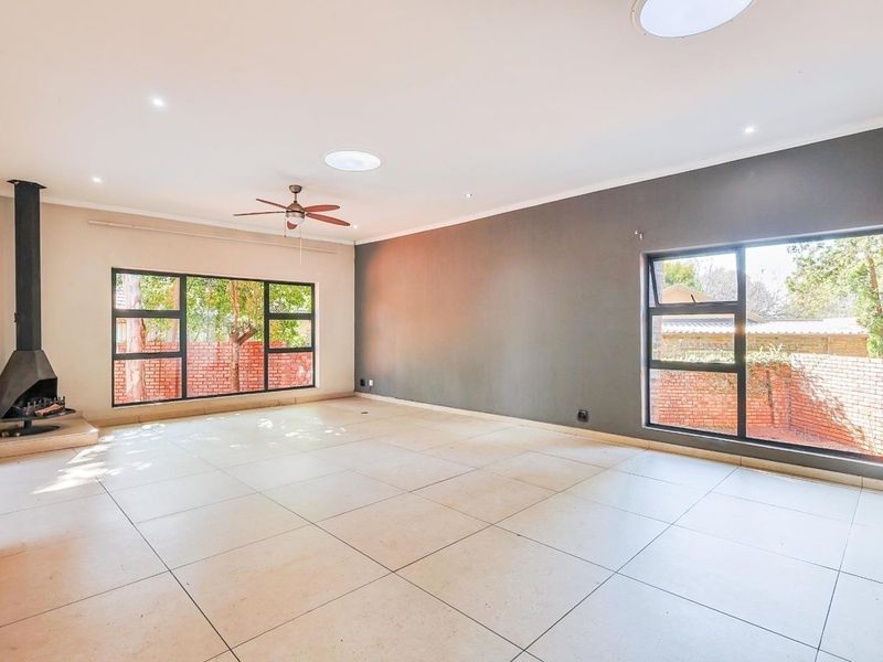 Spacious living area featuring large windows, tiled flooring, a modern freestanding fireplace, and ceiling-mounted skylights, offering a bright and open atmosphere.