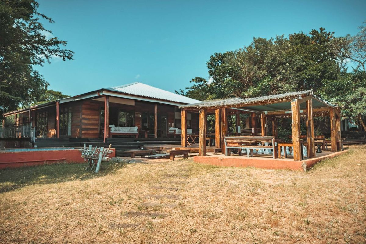 Rear view of a timber-clad house featuring a spacious covered patio, raised wooden decking, and a rustic outdoor pergola area set within a natural garden.