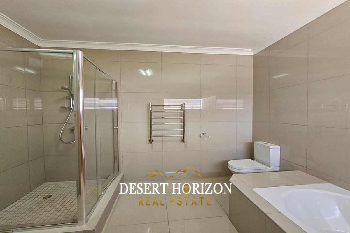 A modern bathroom featuring a glass-enclosed shower, a built-in bathtub, a toilet, and a wall-mounted heated towel rail with neutral tiled finishes.