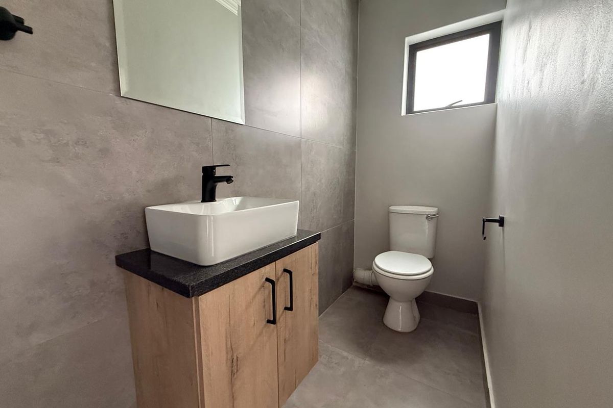 Modern bathroom featuring large-format grey wall tiles, a contemporary vanity with a vessel sink, black fixtures, and a white toilet.