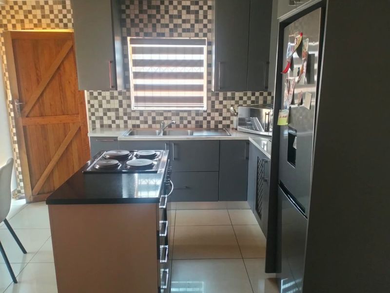 Modern kitchen featuring dark grey cabinetry, a central island with an integrated electric hob, mosaic tile backsplash, and light-colored floor tiles.