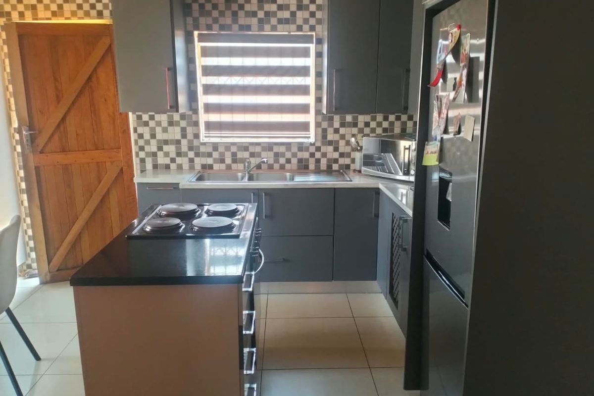 Modern kitchen featuring dark grey cabinetry, a central island with an integrated electric hob, mosaic tile backsplash, and light-colored floor tiles.