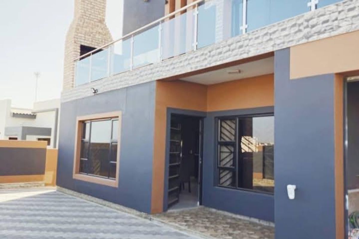 Modern rear exterior view featuring a paved patio area, stone-clad outdoor fireplace, and a balcony with a contemporary glass balustrade.