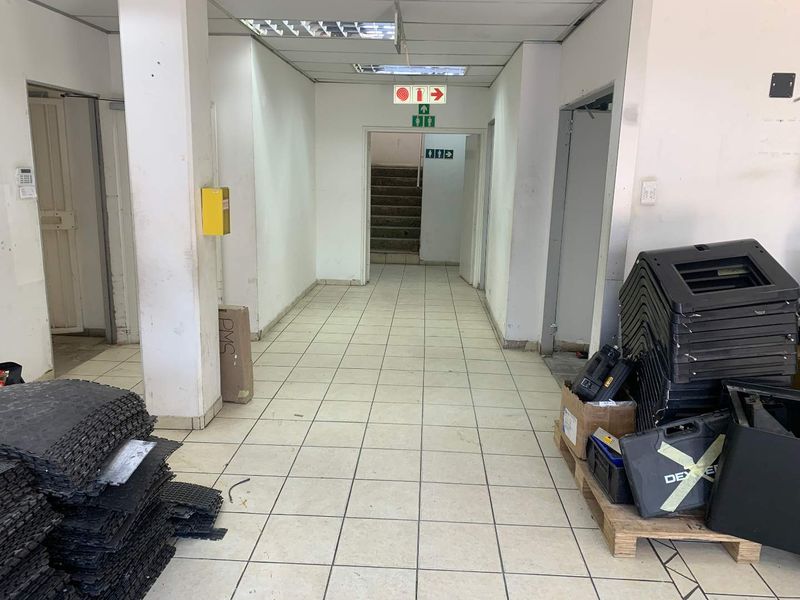A functional industrial hallway featuring ceramic tiled flooring, suspended ceiling panels, and direct access to a staircase and adjacent utility areas.