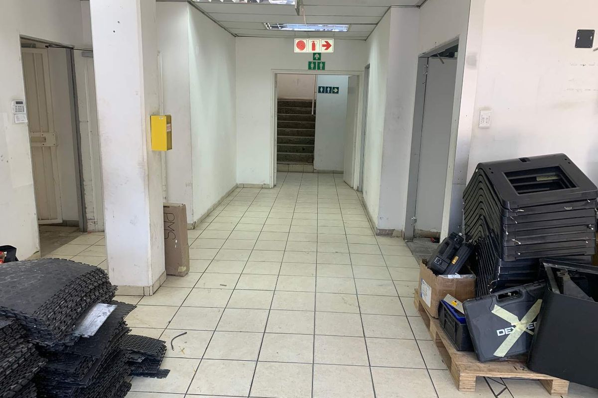 A functional industrial hallway featuring ceramic tiled flooring, suspended ceiling panels, and direct access to a staircase and adjacent utility areas.