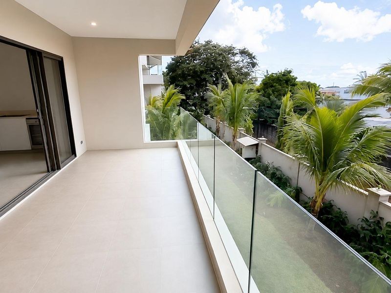 A spacious, modern balcony featuring sleek glass balustrades, neutral floor tiles, and seamless access to the interior living area.