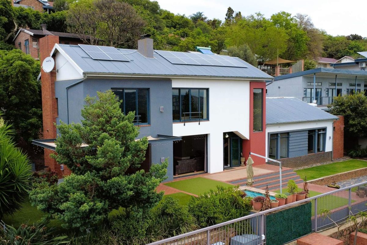 Aerial view of a modern two-story house featuring solar panels, a metal roof, and a landscaped garden with a small pool area.