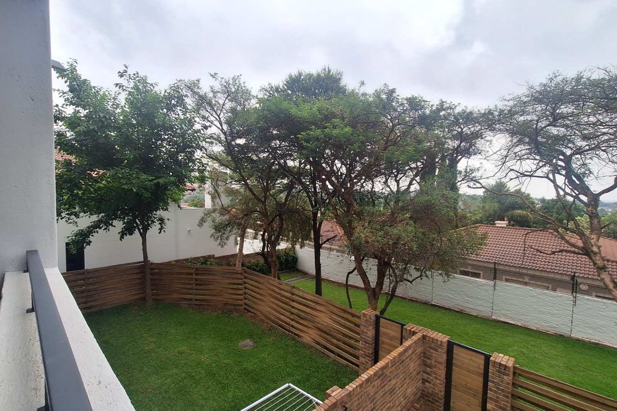 A view from an elevated balcony overlooking a private rear garden with a well-maintained lawn, mature trees, and secure perimeter fencing.