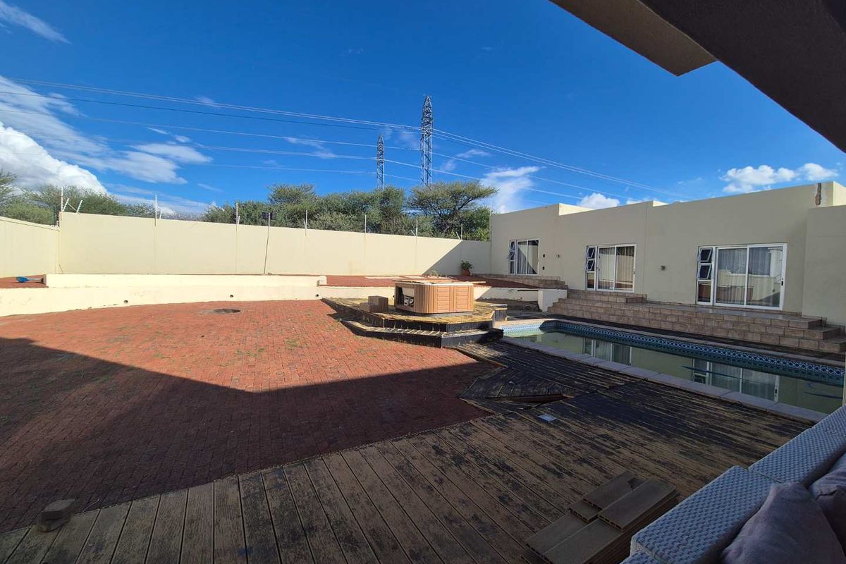 Spacious rear garden featuring a swimming pool, built-in spa, and timber decking area, enclosed by high perimeter walls.