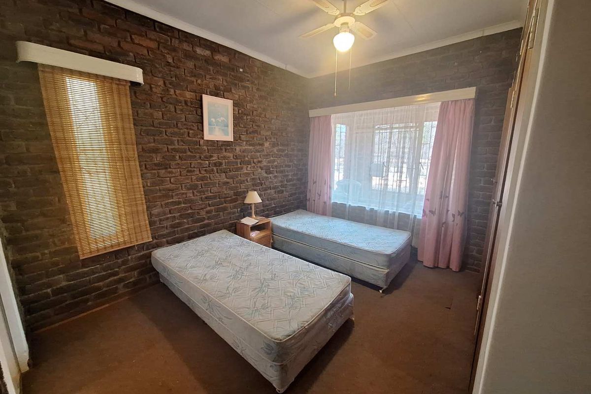 A bedroom featuring exposed brick walls, a ceiling fan, and built-in cupboards, offering a functional space with potential for modernization.