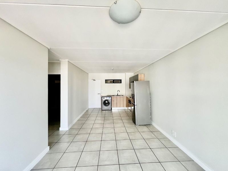An open-plan living and kitchen area featuring neutral tiled flooring, minimalist cabinetry, and a functional layout suitable for modern apartment living.