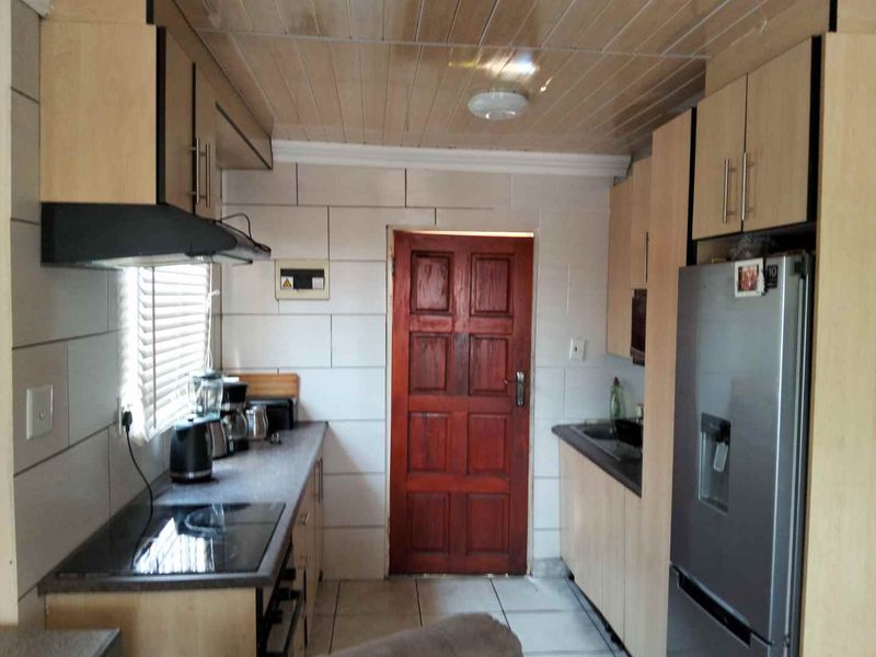 A functional galley-style kitchen featuring built-in cabinetry, laminate countertops, an electric hob with extractor fan, and tiled finishes throughout.
