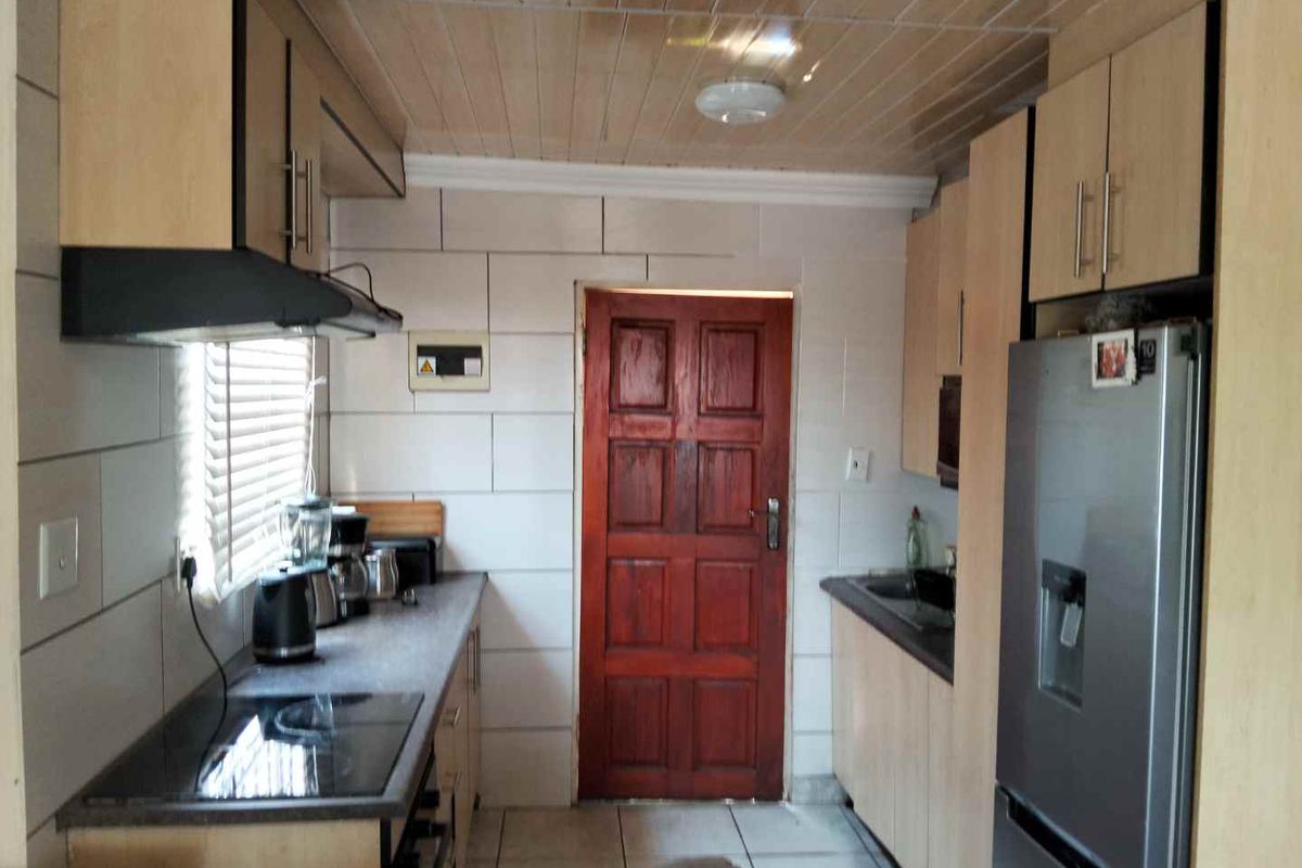 A functional galley-style kitchen featuring built-in cabinetry, laminate countertops, an electric hob with extractor fan, and tiled finishes throughout.