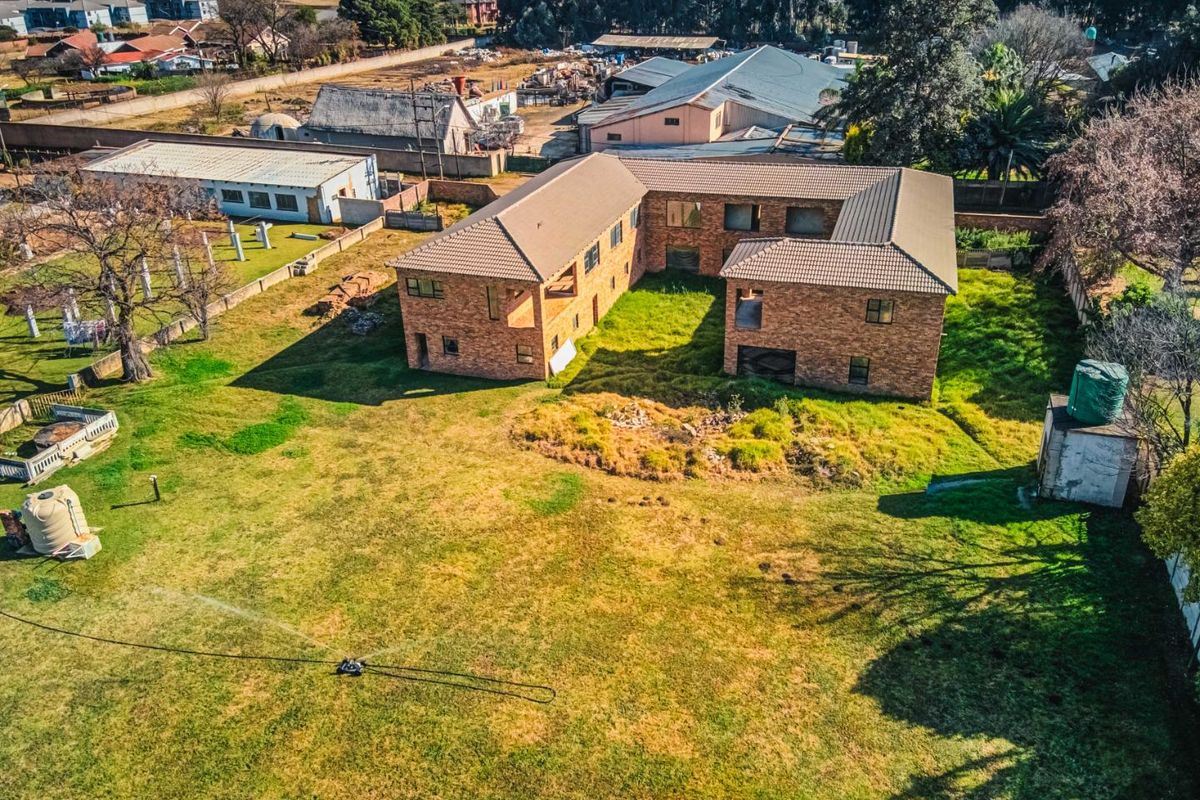 Aerial view of a large facebrick property on a spacious plot with a tiled roof, water storage tank, and extensive lawn area.