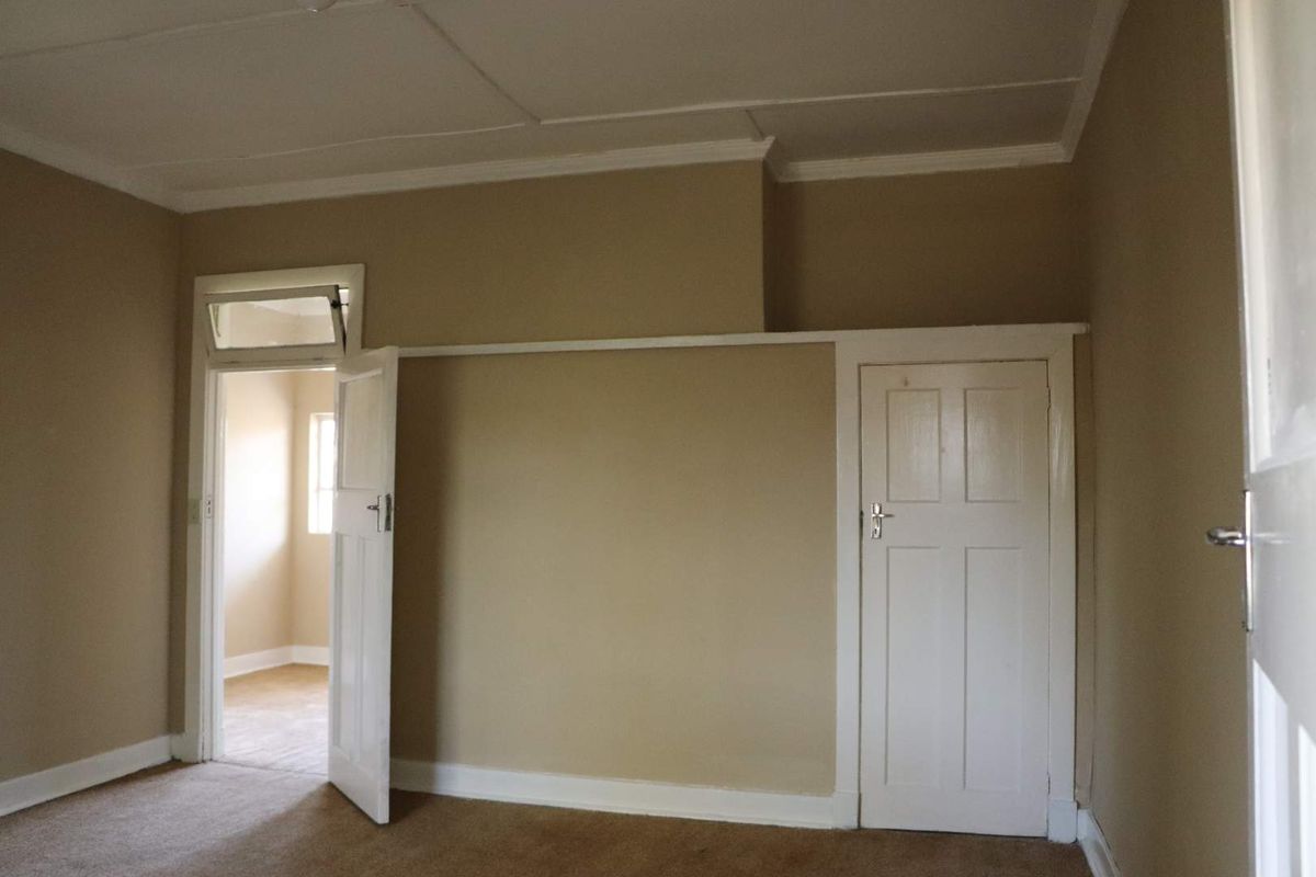 An empty bedroom featuring beige walls, carpeted flooring, and traditional white timber doors with transom windows.