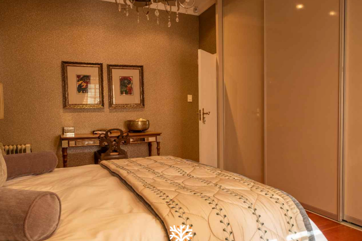 A well-maintained bedroom featuring built-in sliding door wardrobes, crown molding, and warm textured wall finishes.