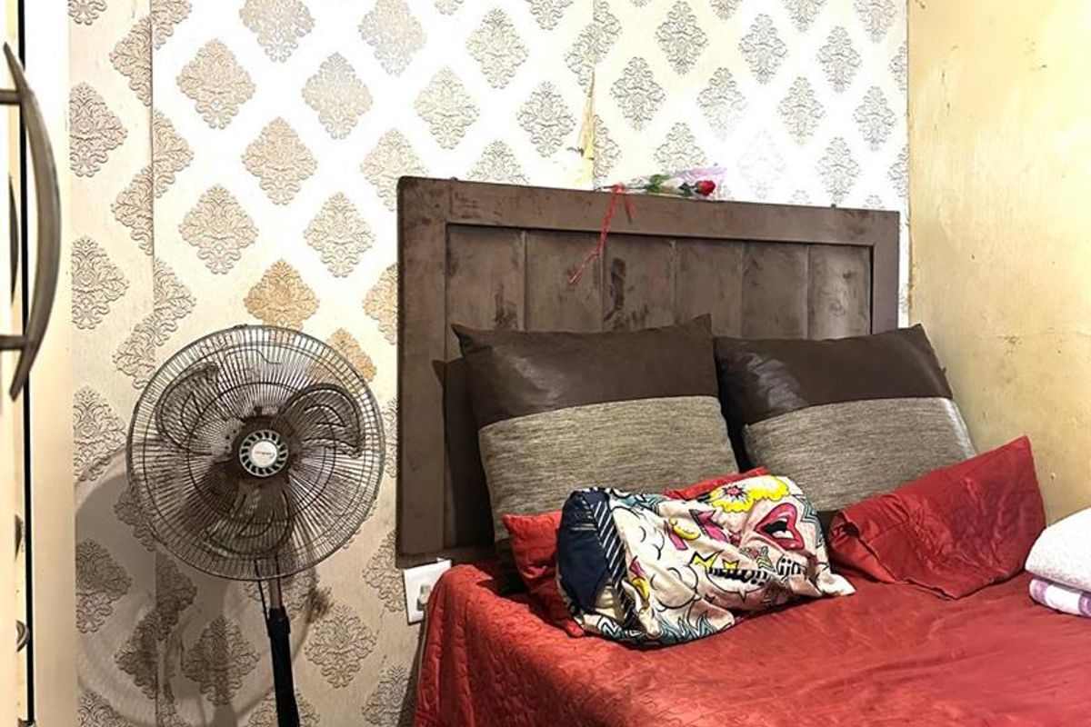 A bedroom featuring patterned wallpaper, a built-in headboard, and tiled flooring, showing signs of wear and requiring cosmetic updates.