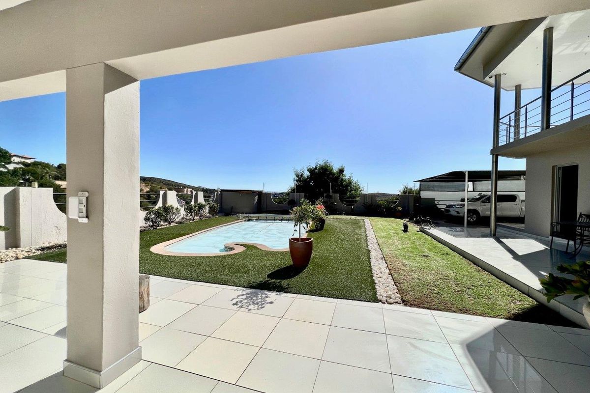 A spacious covered patio overlooking a well-maintained garden area featuring an inground swimming pool and artificial lawn.