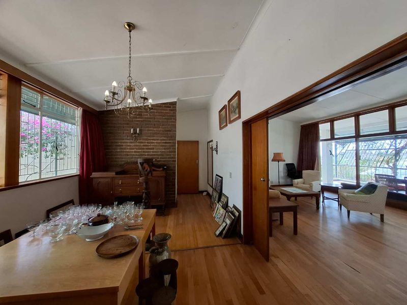 Open plan living and dining area featuring hardwood floors, an exposed brick feature wall, and large windows with security bars.