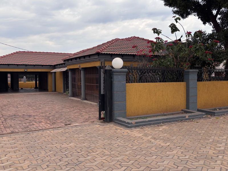 Front view of the property featuring a paved driveway, secure perimeter wall with gate, and a tiled roof structure.