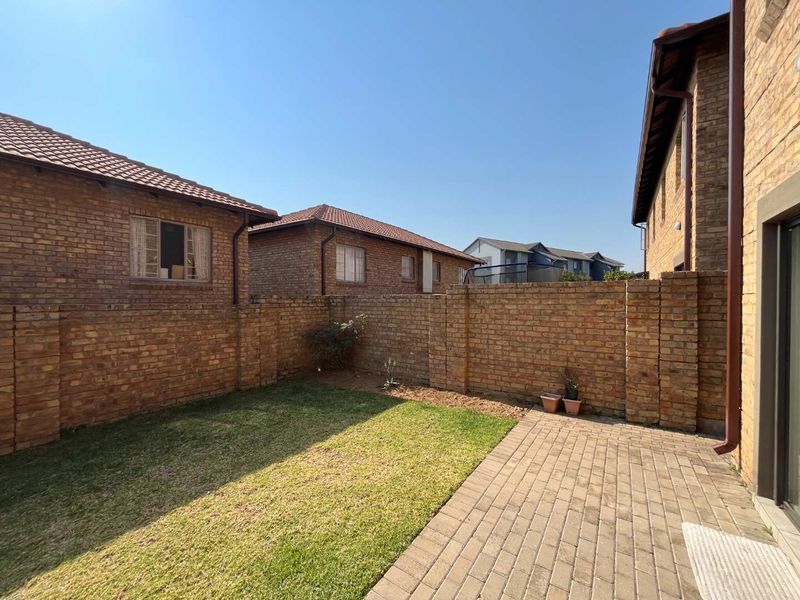 A private rear garden featuring a paved patio area, a small lawn, and enclosed by face brick boundary walls.