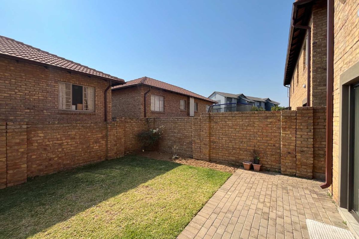 A private rear garden featuring a paved patio area, a small lawn, and enclosed by face brick boundary walls.