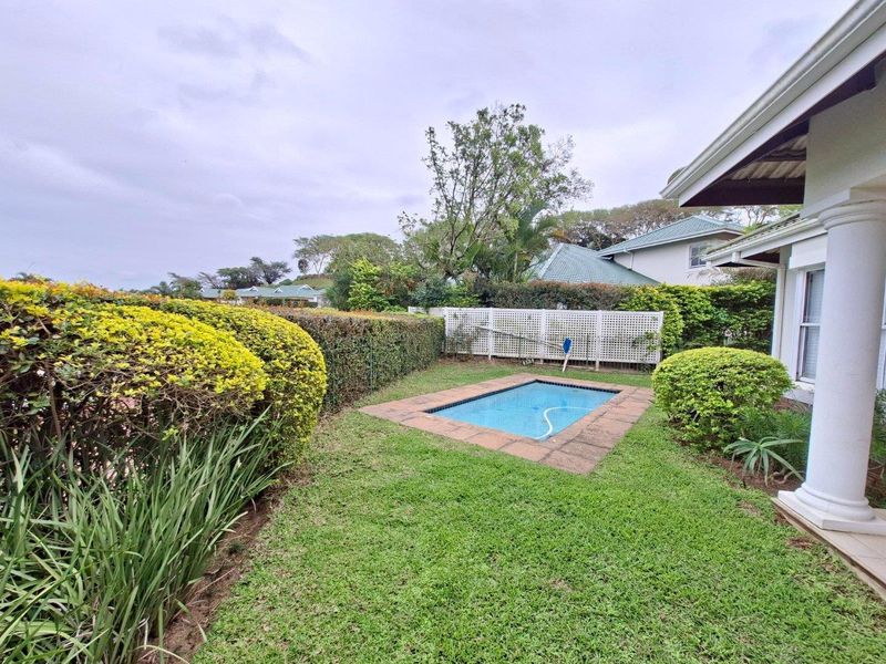 A private garden area featuring a small swimming pool, manicured hedging, and a covered patio space with a structural column.