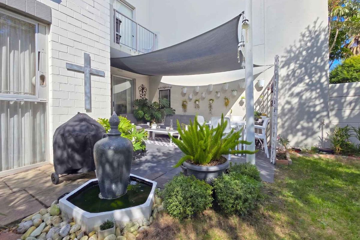 A private rear patio area featuring a paved floor, shade sail, and a decorative water feature, providing a comfortable outdoor living space.