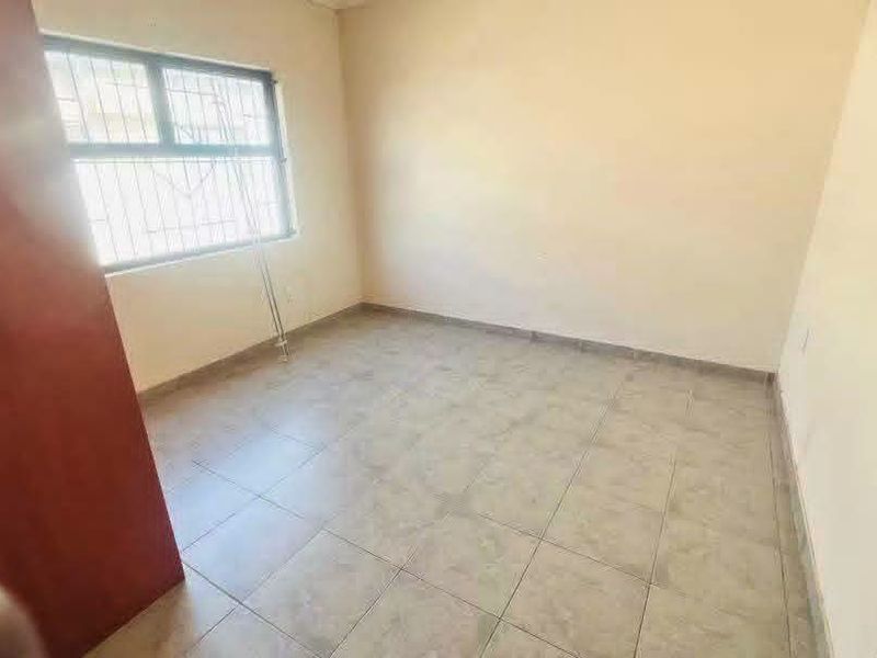 An empty bedroom featuring tiled flooring, a window with security bars, and a built-in cupboard.