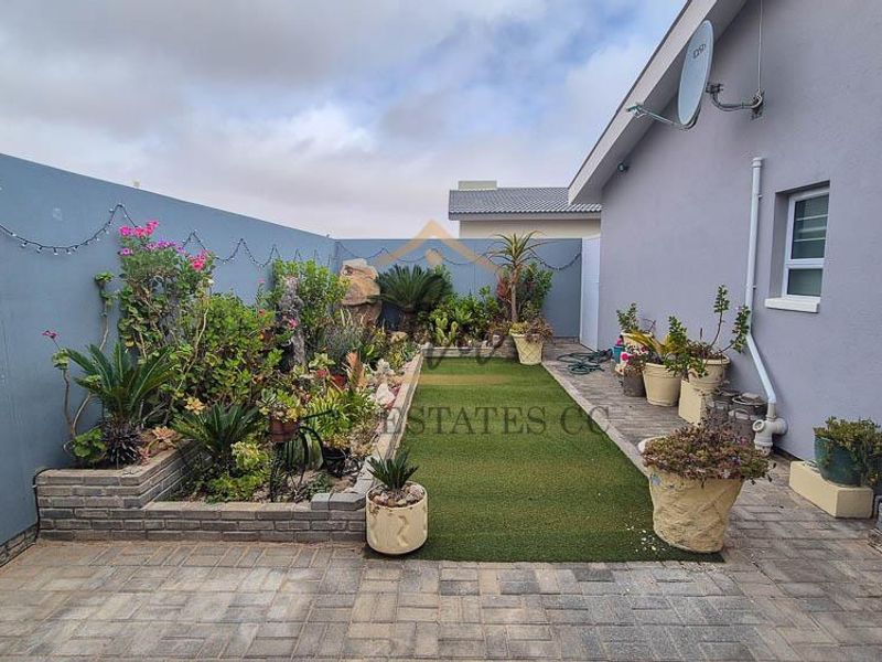 A private rear courtyard featuring brick paving, a raised garden bed, and an artificial lawn area, enclosed by a solid boundary wall.