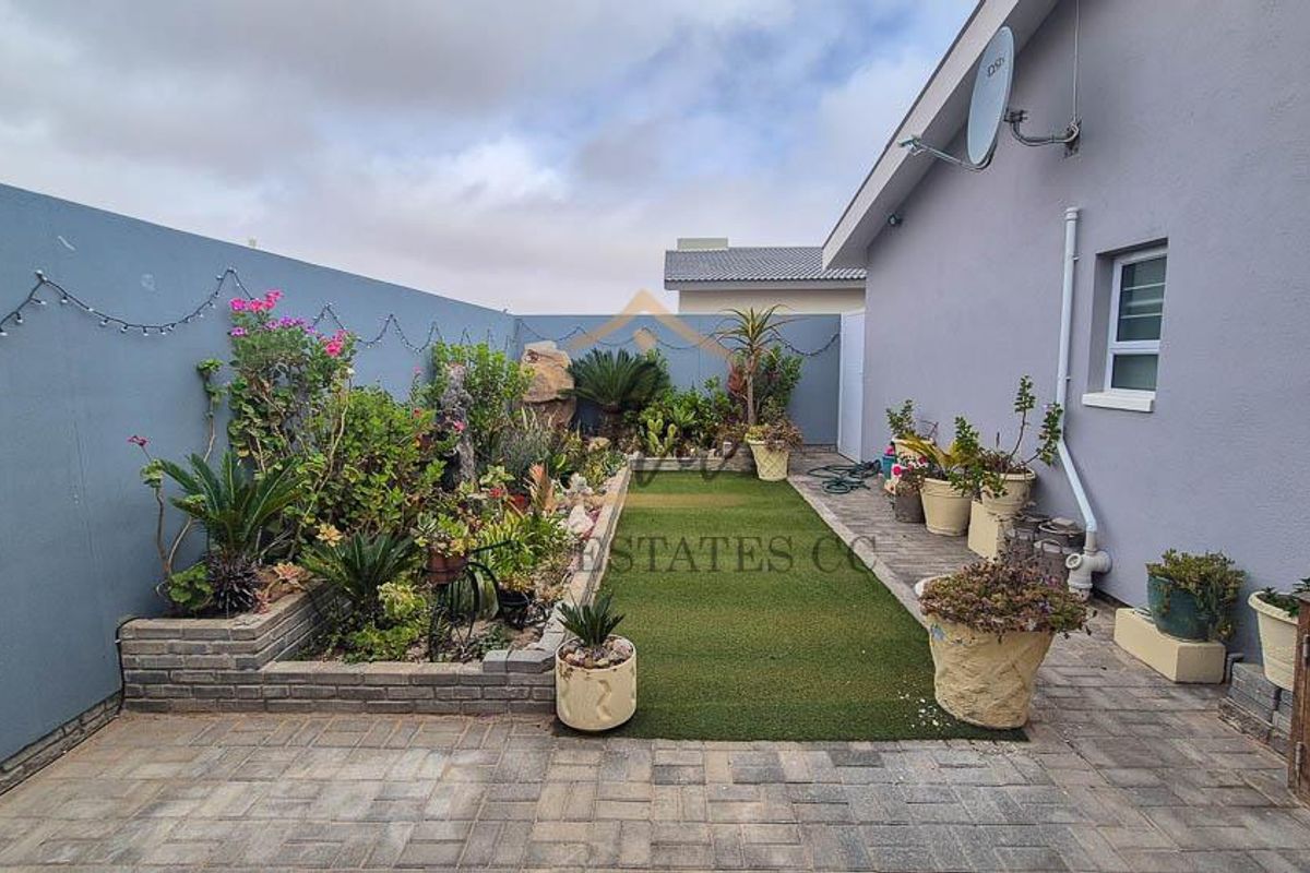 A private rear courtyard featuring brick paving, a raised garden bed, and an artificial lawn area, enclosed by a solid boundary wall.