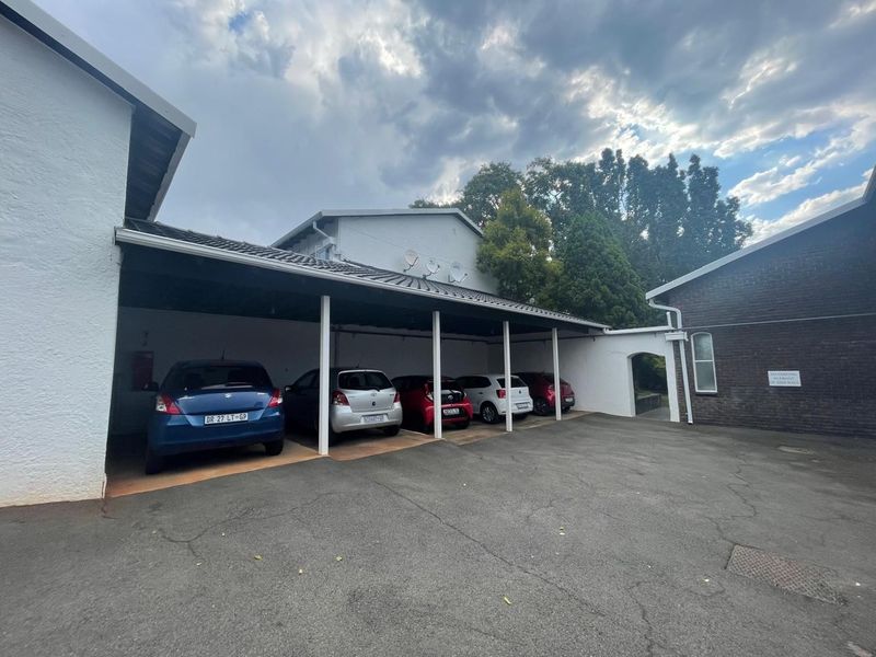 A covered parking area featuring multiple bays with a tiled roof structure and an asphalt driveway.