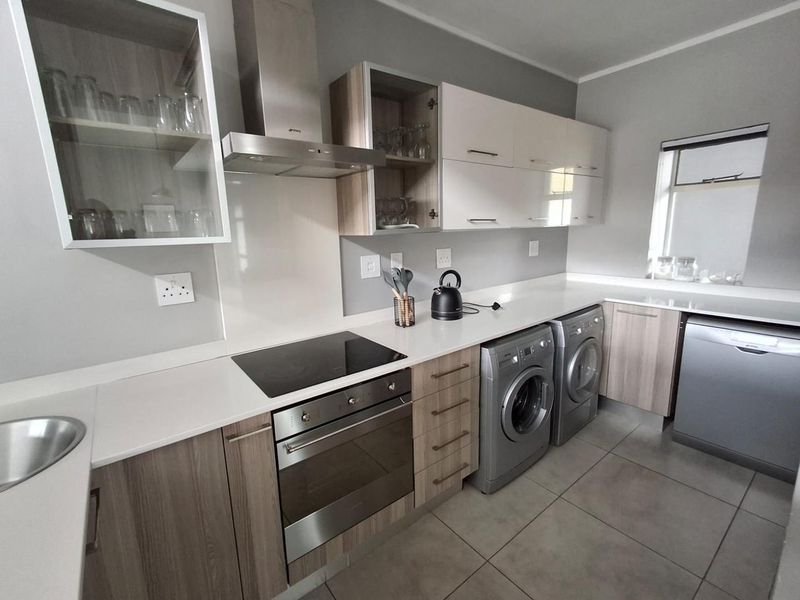Modern kitchen featuring sleek cabinetry, stone countertops, integrated appliances, and tiled flooring, offering a functional and contemporary cooking and laundry space.