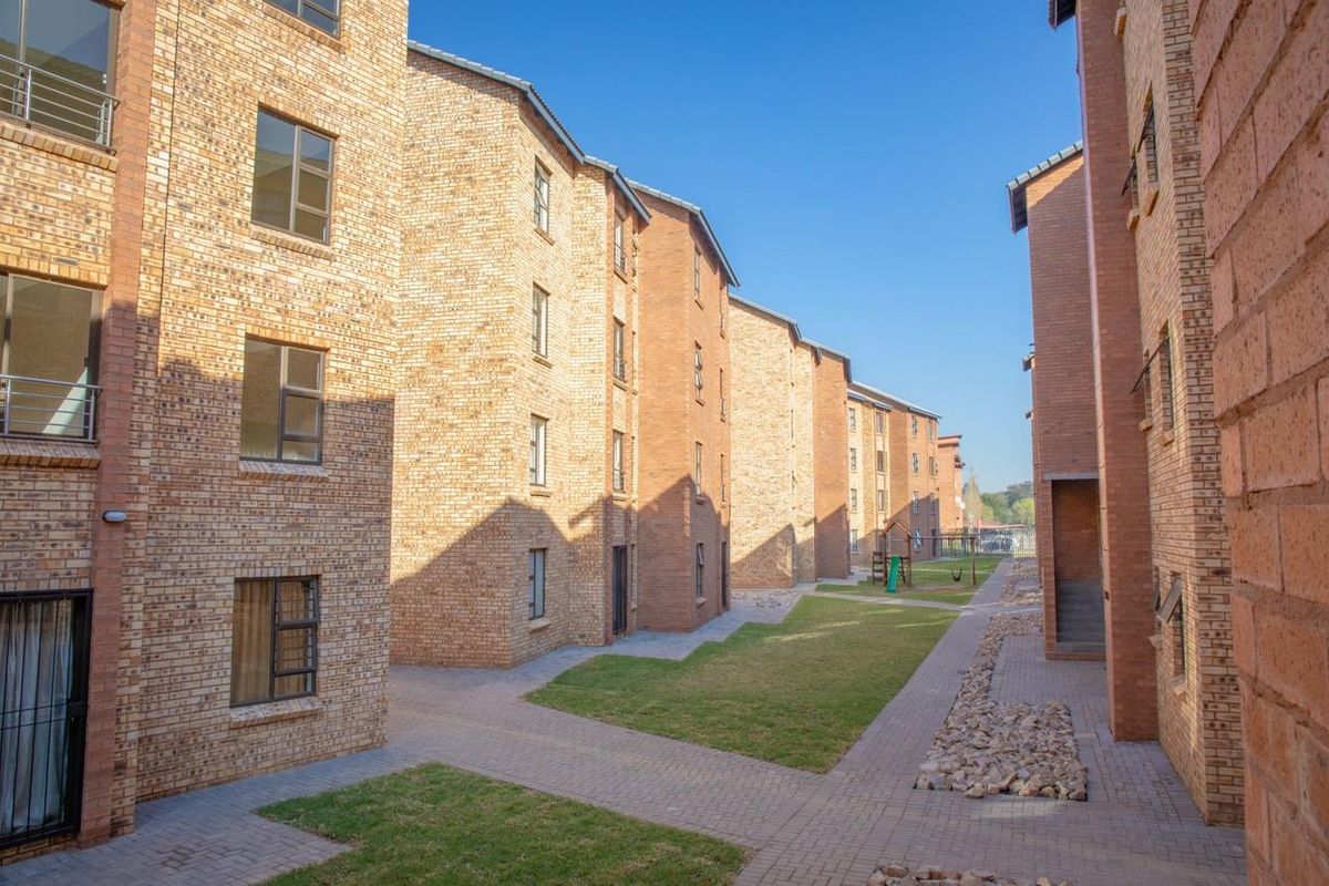 Exterior view of a multi-story apartment complex featuring face brick facades, paved walkways, and communal garden areas.