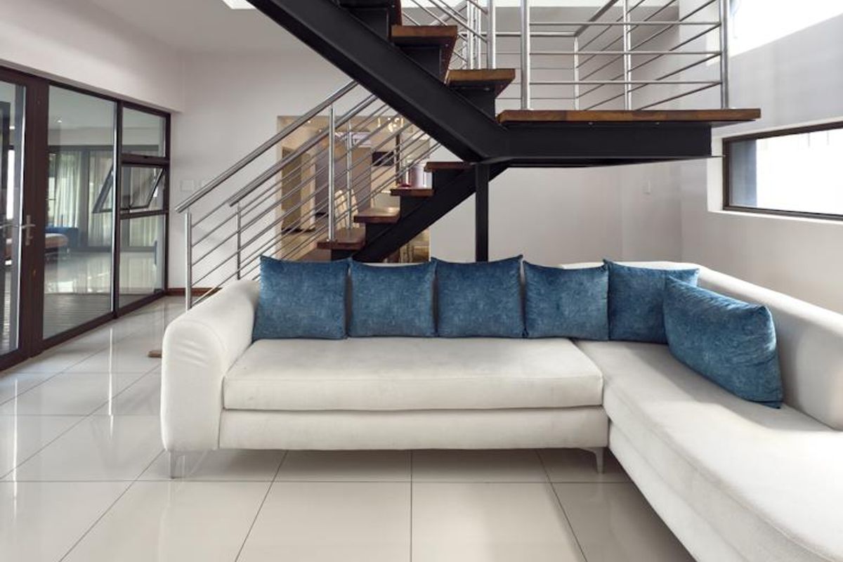 Modern living area featuring a striking open-tread staircase with steel and timber finishes, complemented by large format floor tiles and expansive windows.