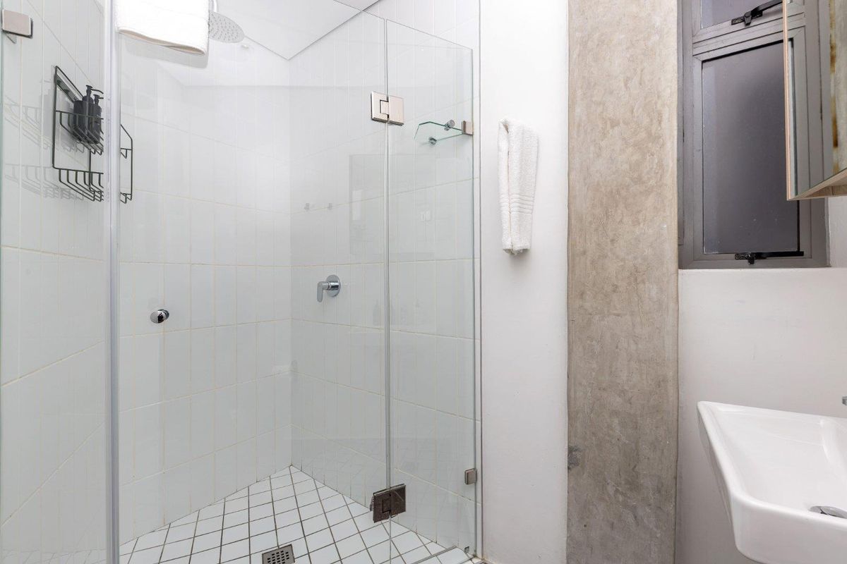 Modern bathroom featuring a glass-enclosed shower with white tiled walls, a mosaic tiled floor, and a sleek wall-mounted basin.