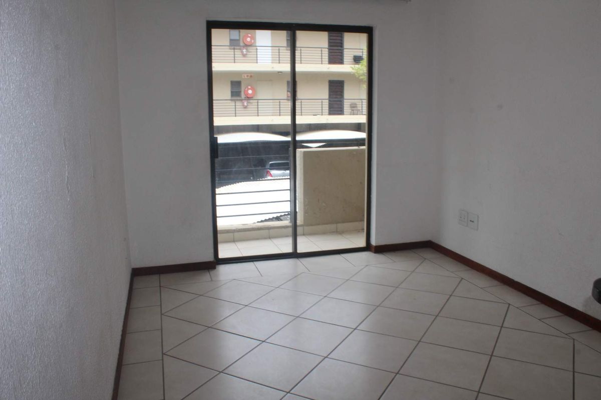 An empty living room featuring neutral tiled flooring and a sliding glass door providing access to a balcony.