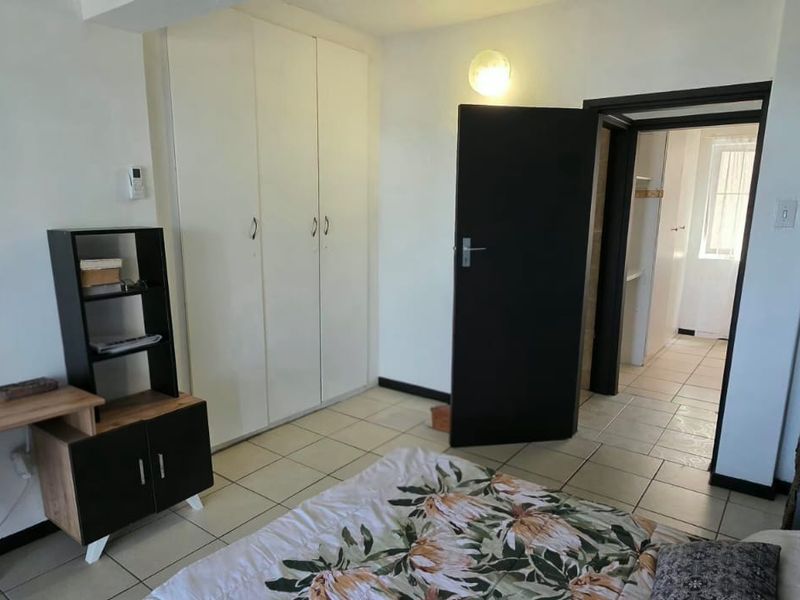 A bedroom featuring tiled flooring and built-in cupboards, with an adjoining doorway leading to a secondary space.