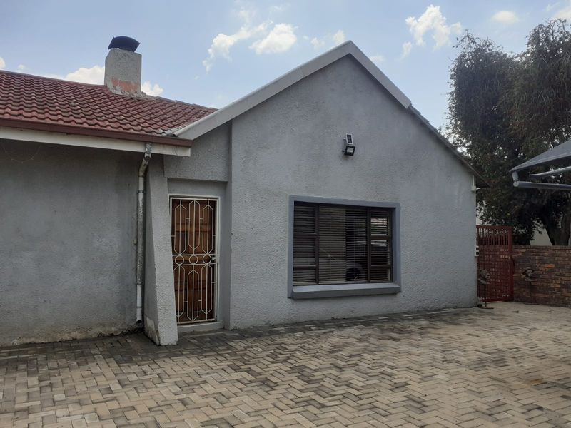 Front exterior view of the cottage featuring a paved driveway, tiled roof, chimney, and secure entrance with a metal security gate.