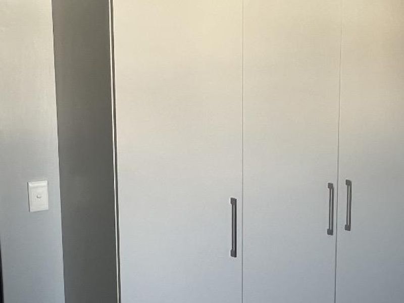 A clean bedroom featuring a modern built-in wardrobe and a wall-mounted split-system air conditioning unit.