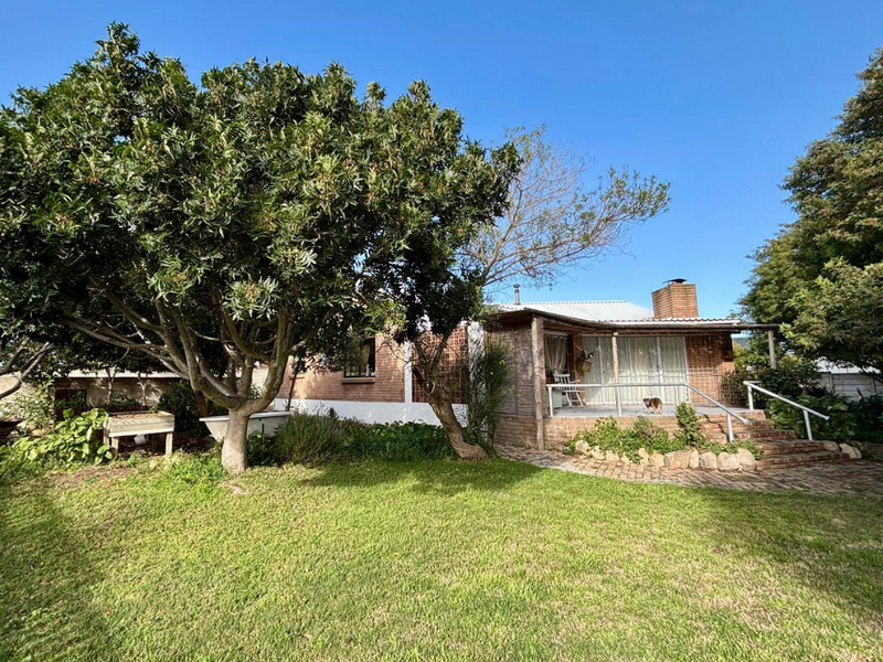 Rear view of the house featuring a covered patio, brick chimney, and established garden with mature trees and brick paved pathways.