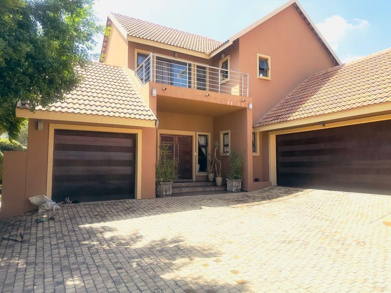 A double-story residential property featuring a paved driveway, two double garages, and an upper-level balcony with stainless steel railings.